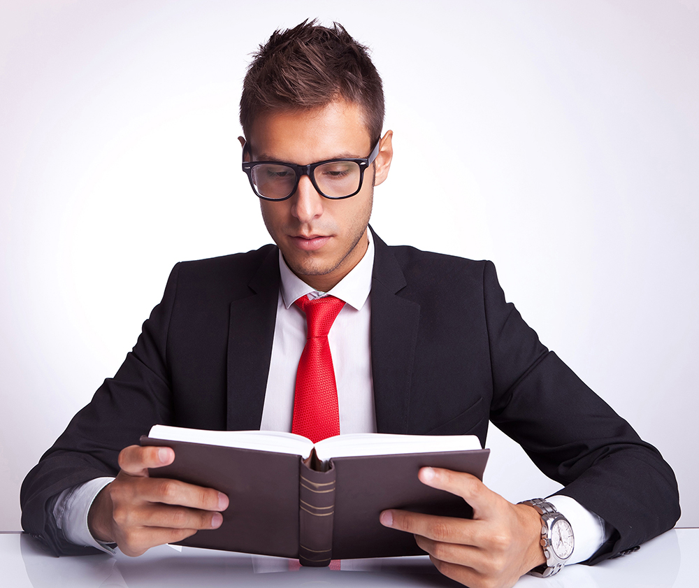 young business man wearing glasses reading a book at his office desk